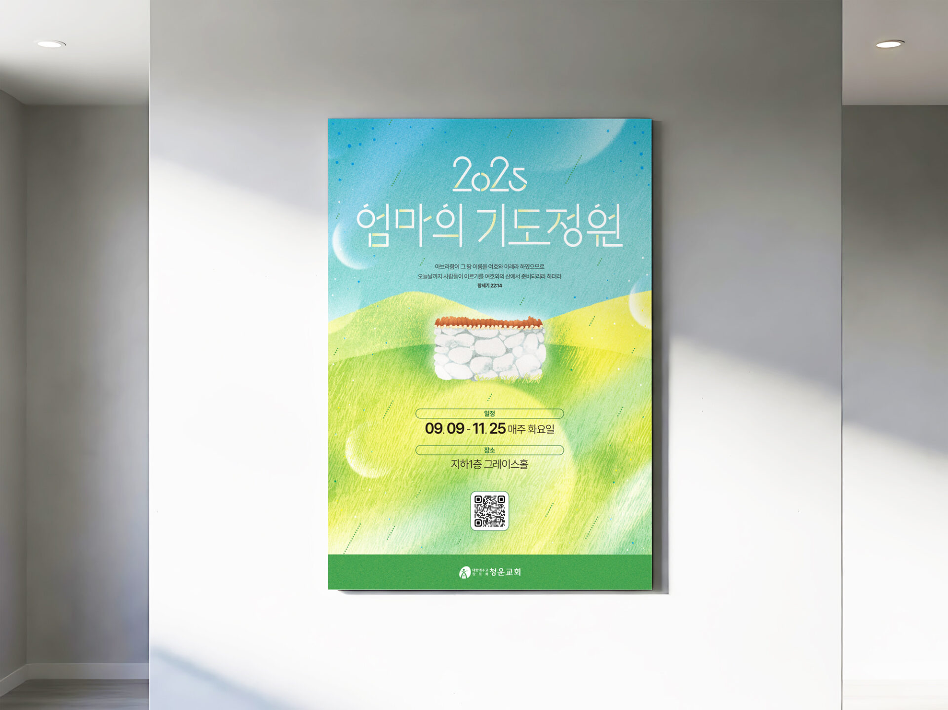 흰 실내 벽에 엄마의 기도정원 포스터가 걸려 있고 위쪽에서 들어온 햇빛이 벽과 포스터 위에 비스듬히 비칩니다.